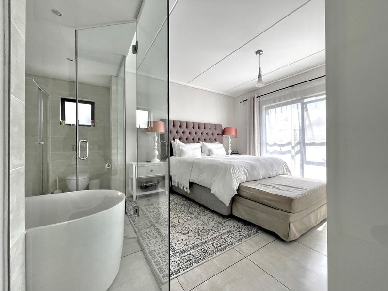 Modern bedroom featuring an open-plan en-suite bathroom with a freestanding bathtub and glass shower enclosure, complemented by tiled floors and natural light.