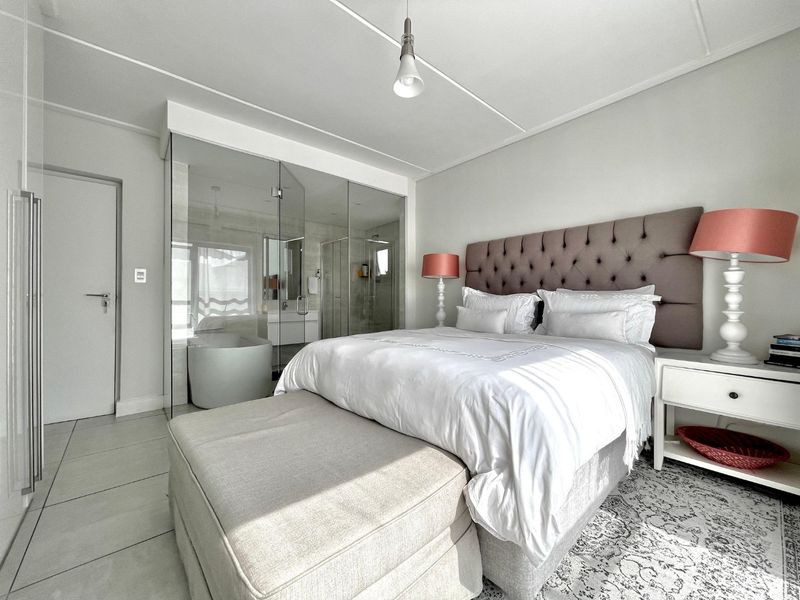 Modern bedroom featuring tiled flooring and a contemporary glass-enclosed en-suite bathroom, creating an open and bright living space.