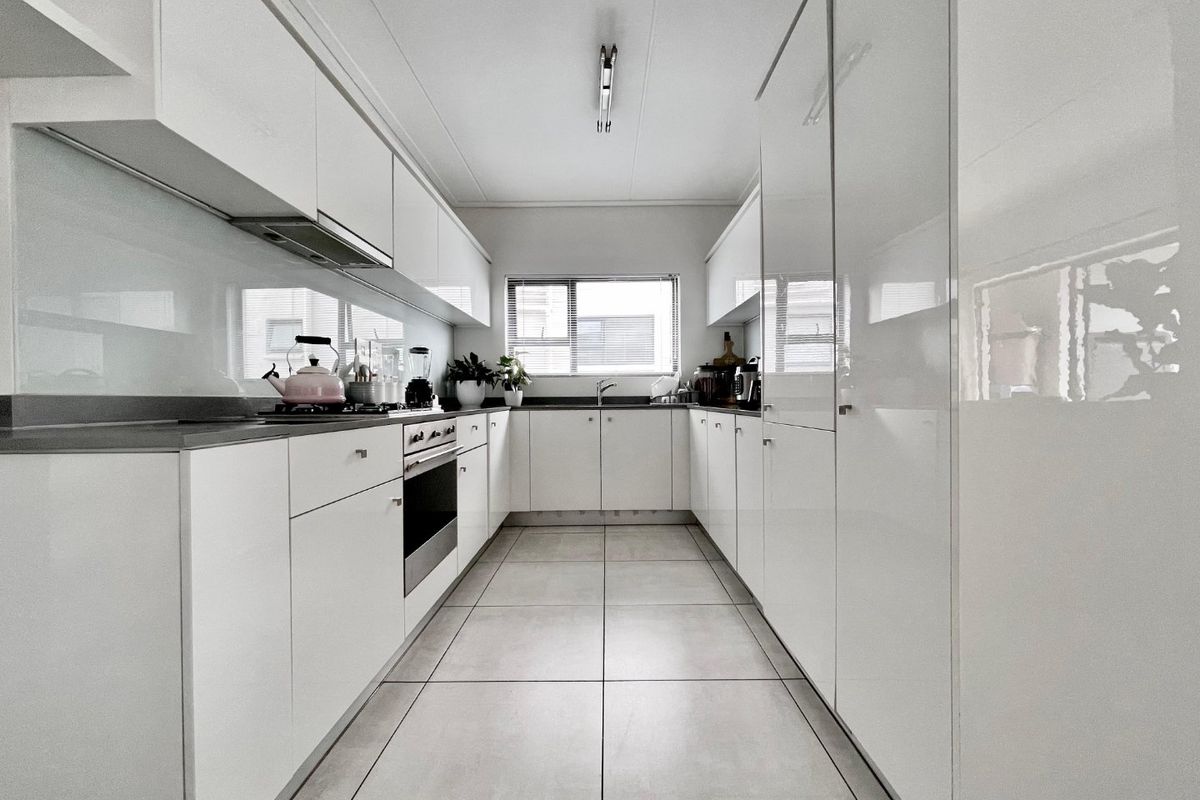 Modern galley-style kitchen featuring high-gloss white cabinetry, integrated appliances, sleek glass splashbacks, and neutral floor tiles.