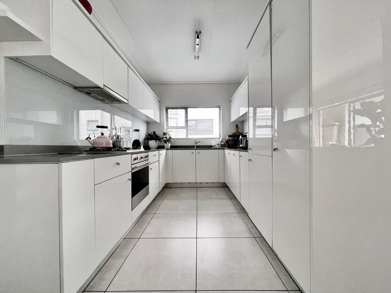 Modern galley-style kitchen featuring high-gloss white cabinetry, integrated appliances, sleek glass splashbacks, and neutral floor tiles.