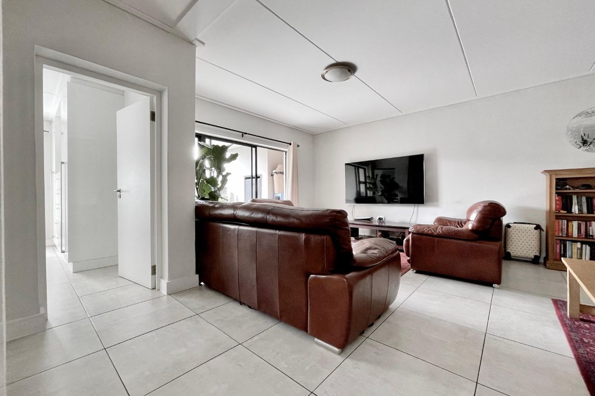 A bright living room featuring neutral tiled flooring, a sliding glass door providing natural light, and a clean, minimalist ceiling design.