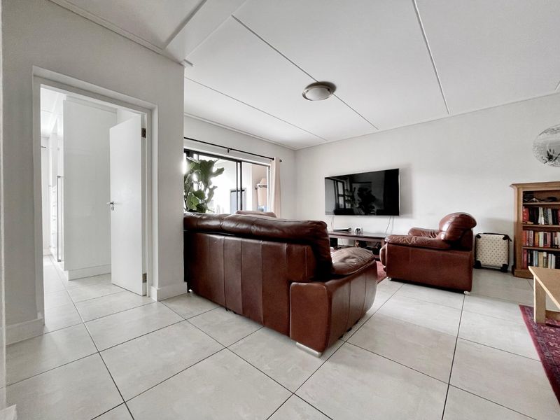 A bright living room featuring neutral tiled flooring, a sliding glass door providing natural light, and a clean, minimalist ceiling design.