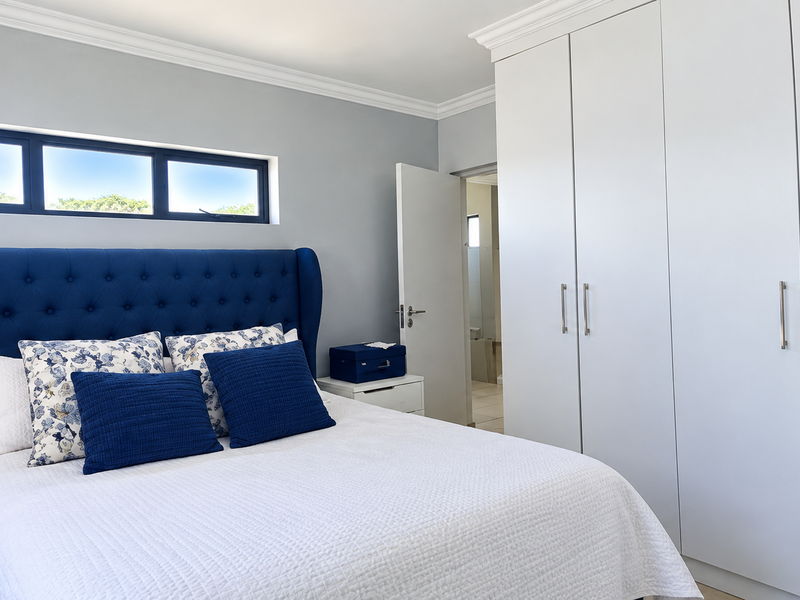 A well-maintained bedroom featuring built-in cupboards, decorative cornice, and a modern horizontal window, offering a clean and bright living space.
