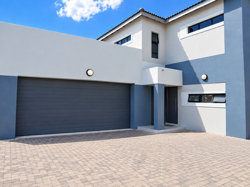 Modern double-storey residential property featuring a paved driveway, integrated double garage, and contemporary two-tone exterior facade with secure boundary walling.