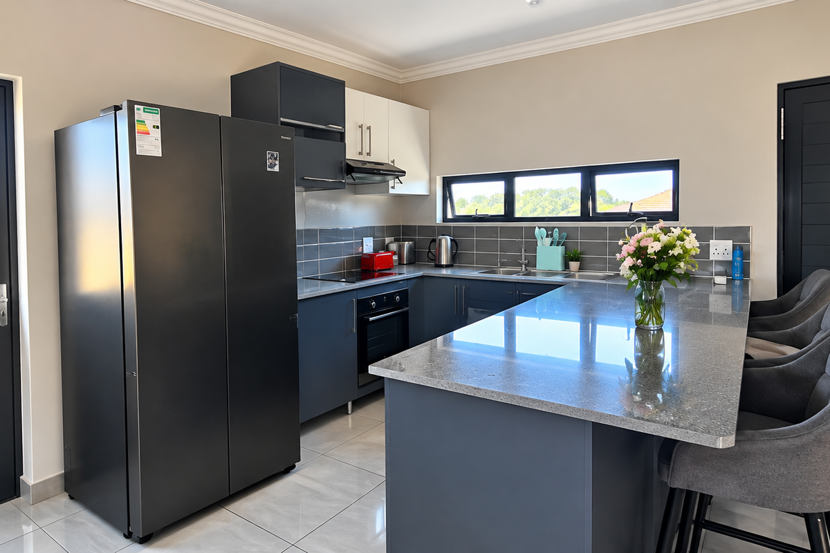 Modern kitchen featuring dark cabinetry, granite countertops, a central island, and high-quality built-in appliances, complemented by sleek tiled flooring and natural light.