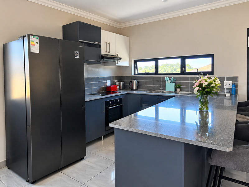 Modern kitchen featuring dark cabinetry, granite countertops, a central island, and high-quality built-in appliances, complemented by sleek tiled flooring and natural light.