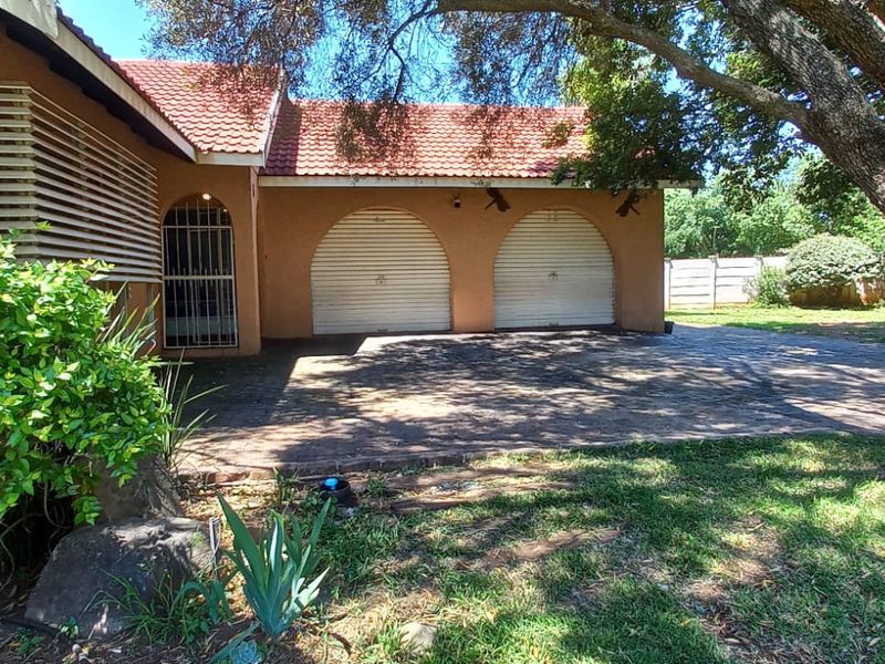 Front view of a residential property featuring a double garage with arched doors, a paved driveway, and mature garden landscaping.