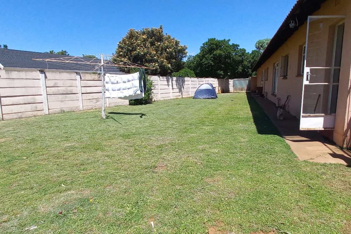 A spacious rear garden featuring a large lawn area, enclosed by precast concrete boundary walls and accessible via a side security gate.