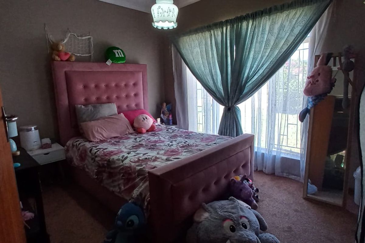 A standard bedroom featuring carpeted flooring and a window fitted with security bars, providing natural light.