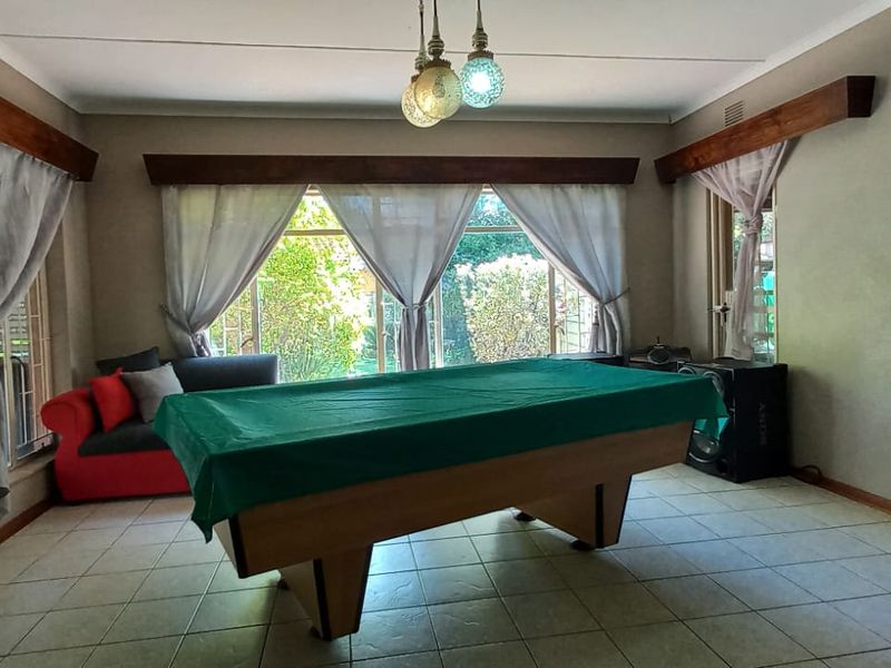 Spacious living area featuring tiled flooring, large windows with timber pelmets, and pendant lighting, offering a versatile space for relaxation or entertainment.