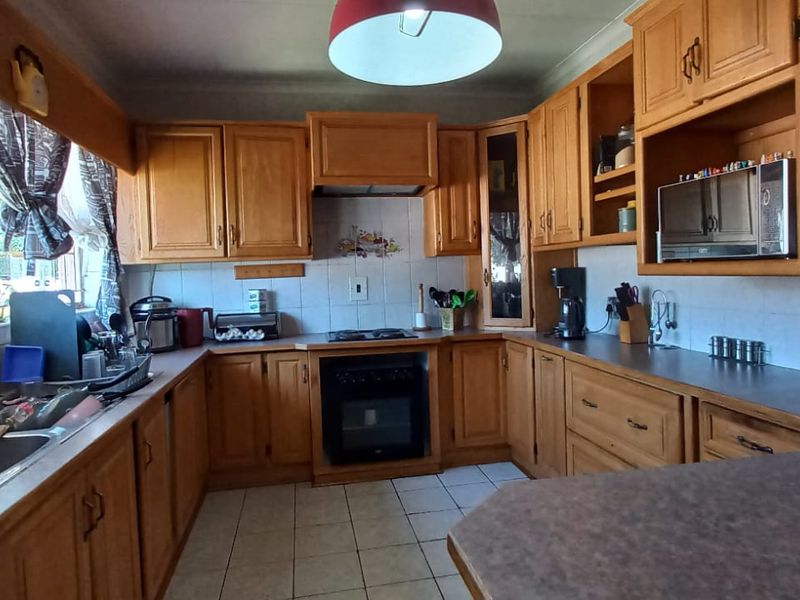 A functional kitchen featuring traditional wooden cabinetry, tiled backsplash, built-in oven and hob, and ample laminate countertop workspace.