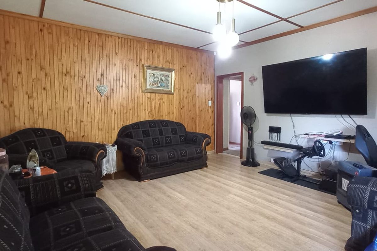 Living room featuring wood paneling, laminate flooring, and an exposed beam ceiling.