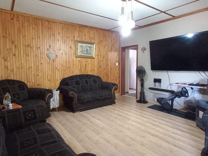 Living room featuring wood paneling, laminate flooring, and an exposed beam ceiling.