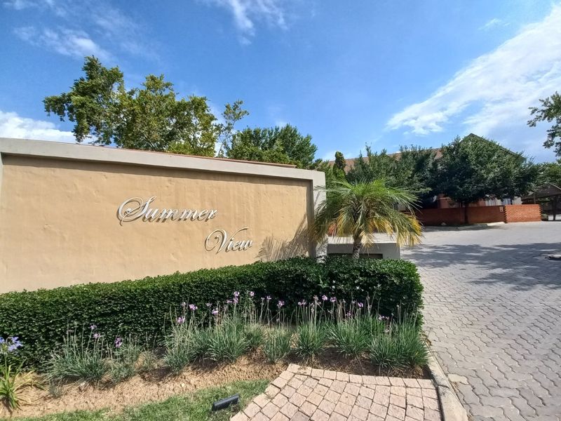 Entrance view of the Summer View complex featuring a prominent boundary wall, paved driveway, and well-maintained landscaped garden area.