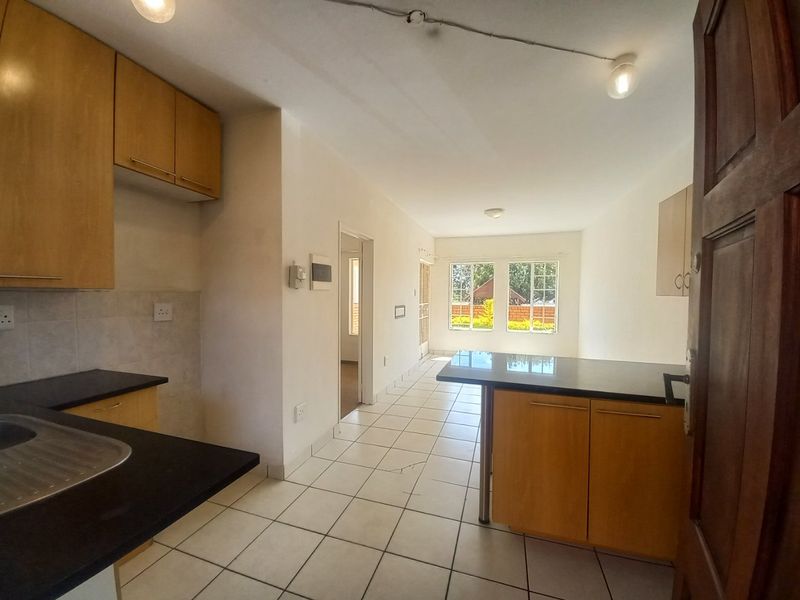Open-plan kitchen and living area featuring light wood cabinetry, dark granite countertops, tiled flooring, and natural light through rear windows.