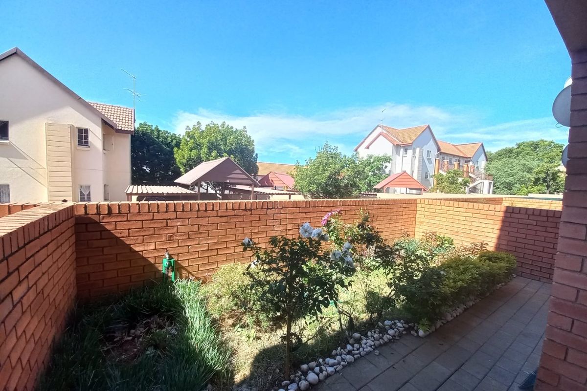 A private rear courtyard featuring a paved patio area, established garden beds, and a secure brick boundary wall.