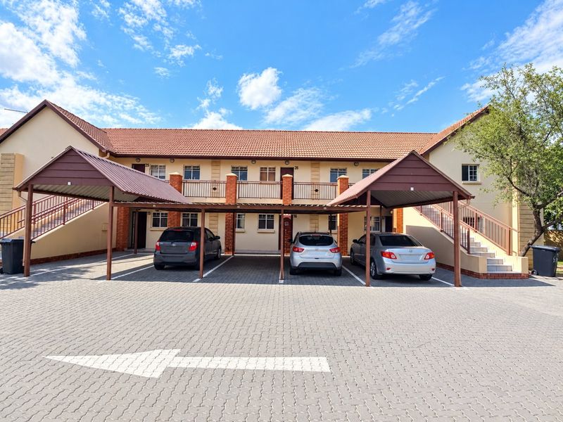 Front view of a well-maintained apartment complex featuring covered parking bays, paved driveway, and external staircases leading to upper-level units.