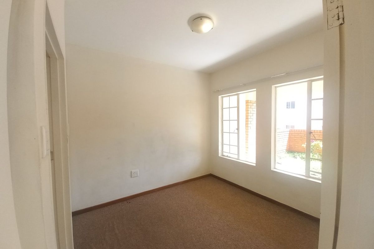 A vacant bedroom featuring carpeted flooring, neutral walls, and dual windows providing natural light and a view of the exterior brickwork.