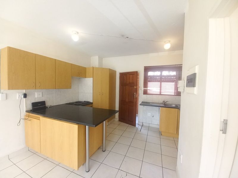 A functional kitchen featuring laminate cabinetry, black countertops, a built-in hob, and tiled flooring, offering a blank canvas for potential renovation.