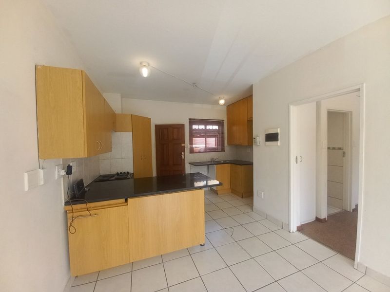 A functional kitchen featuring light wood cabinetry, dark countertops, a built-in hob, and tiled flooring, offering a clean, blank canvas for potential updates.