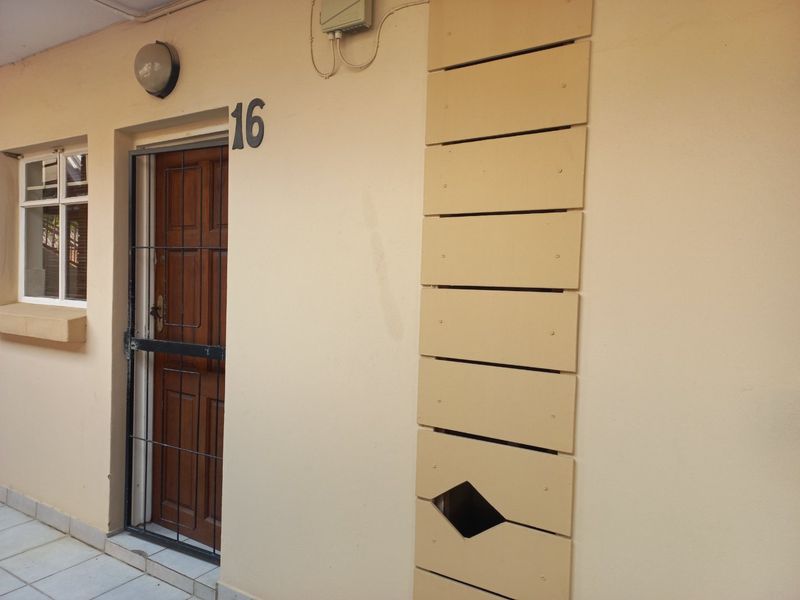 Apartment entrance featuring a wooden door with a security gate and a damaged decorative letterbox panel on the exterior wall.