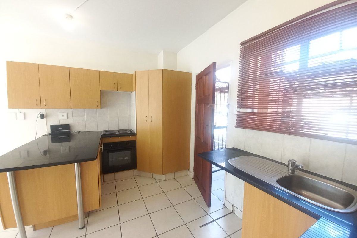A functional kitchen featuring light wood cabinetry, dark laminate countertops, built-in oven and hob, and tiled flooring with direct access to an exterior door.