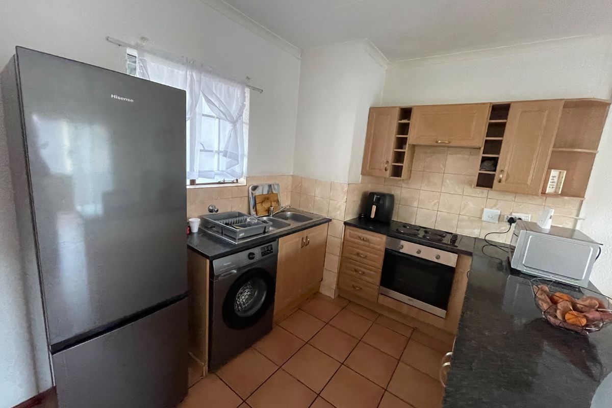 A functional kitchen featuring wooden cabinetry, tiled backsplash, built-in oven and hob, and tiled flooring, offering a practical layout for daily use.