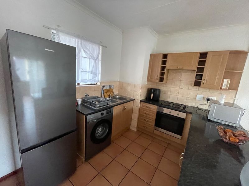 A functional kitchen featuring wooden cabinetry, tiled backsplash, built-in oven and hob, and tiled flooring, offering a practical layout for daily use.