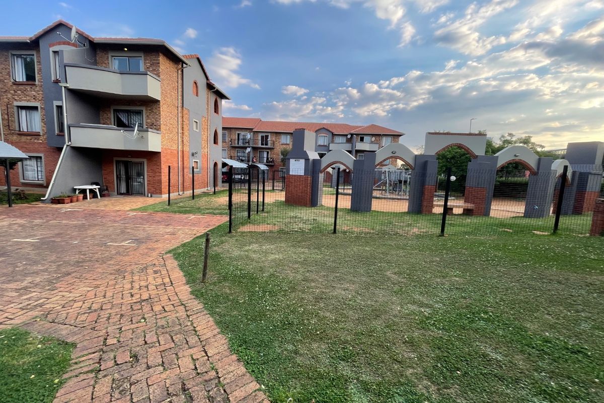 Exterior view of an apartment complex featuring brick facades, balconies, and a communal garden area with paved walkways and decorative archways.