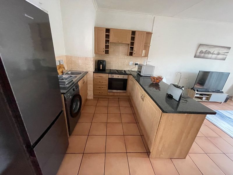 Open plan kitchen featuring light wood cabinetry, granite countertops, built-in oven, hob, and tiled flooring, seamlessly integrated with the living area.