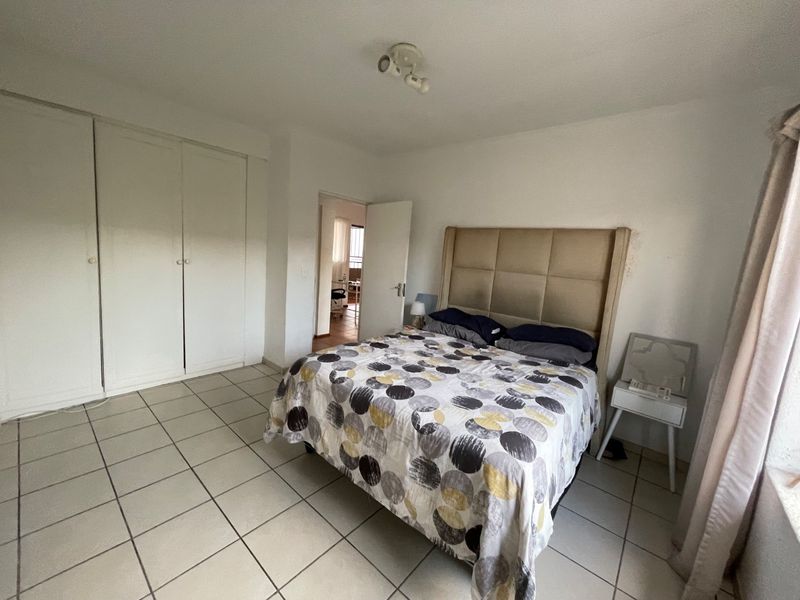A bedroom featuring tiled flooring and built-in cupboards, offering a functional space with neutral finishes.