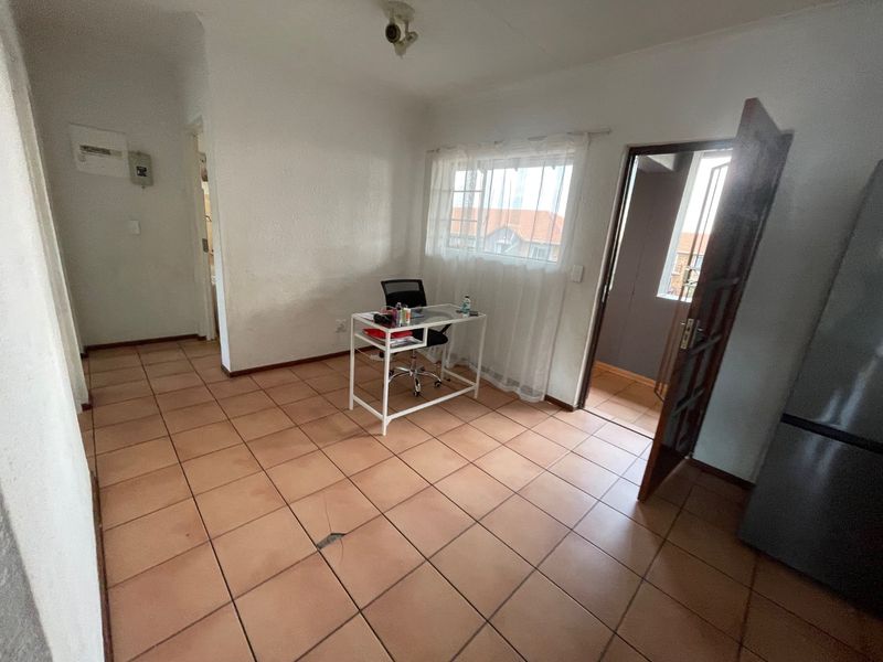 A sparsely furnished living area featuring ceramic floor tiles and a ceiling-mounted light fixture, with a visible crack in the floor tiling.