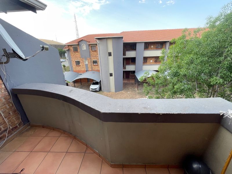 A private balcony with tiled flooring and a parapet wall, overlooking the apartment complex courtyard and covered parking area.