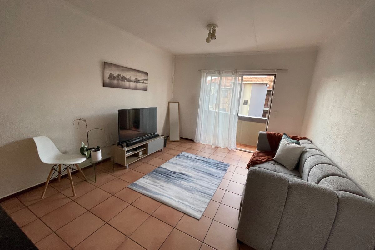 A living room featuring tiled flooring and a sliding glass door providing access to a balcony, offering a functional and well-lit living space.