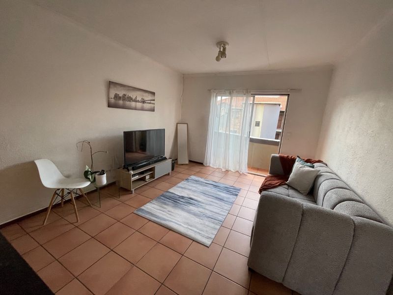 A living room featuring tiled flooring and a sliding glass door providing access to a balcony, offering a functional and well-lit living space.