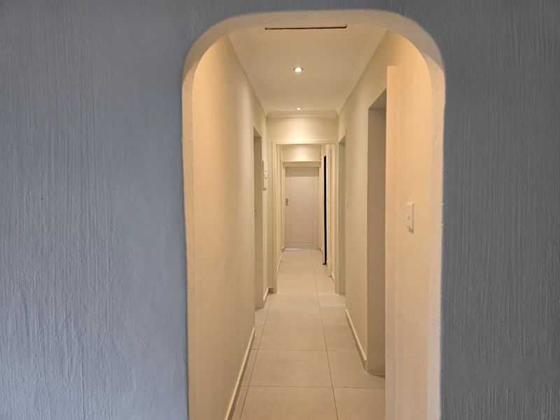 A clean, well-lit hallway featuring an arched entrance, neutral tiled flooring, and recessed ceiling lighting, providing a bright transition between living spaces.