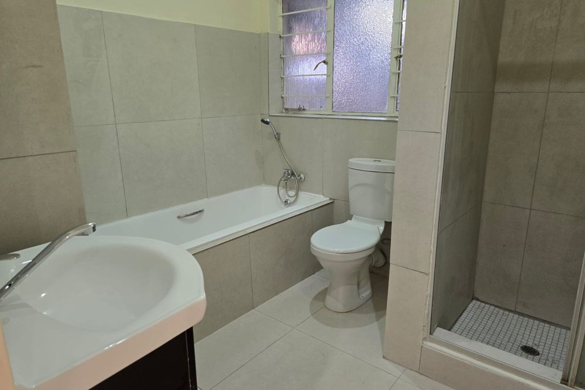A clean, modern bathroom featuring a built-in bathtub, separate shower enclosure, toilet, and vanity basin with neutral wall and floor tiling.