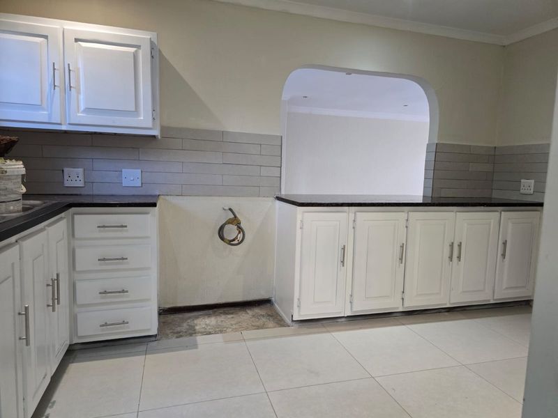 A kitchen featuring white cabinetry, dark granite countertops, and subway tile backsplash, currently awaiting appliance installation in the designated open space.