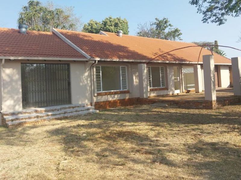 Rear view of the house featuring a brick patio, terracotta tiled roof, and sliding doors with security gates, set against a large garden area.