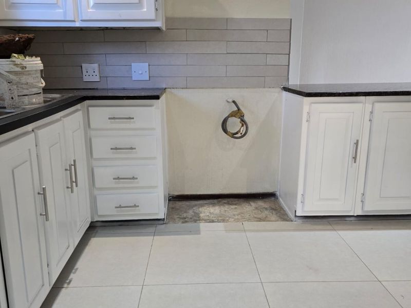 A kitchen area featuring white cabinetry, dark granite countertops, and a tiled backsplash, with a dedicated space for an appliance.