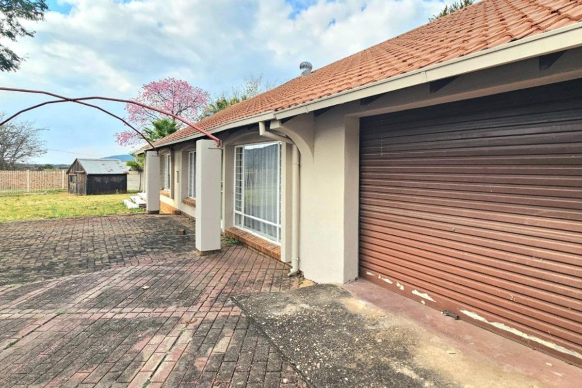 Rear exterior view showing a paved patio area, tiled roof, and a garage with a roller door.