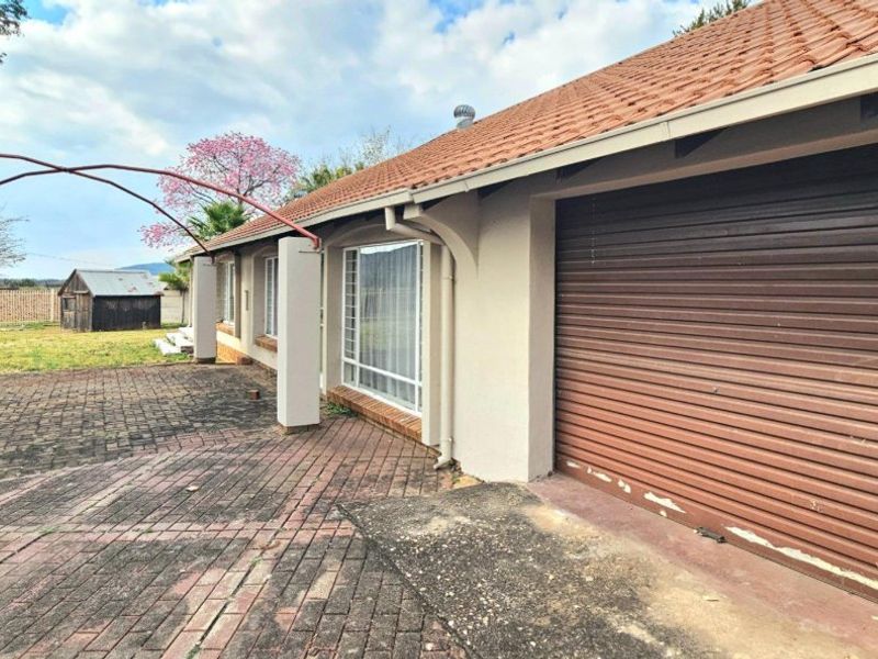Rear exterior view showing a paved patio area, tiled roof, and a garage with a roller door.