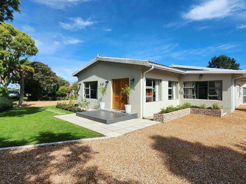 A well-maintained single-story house featuring a tiled entrance porch, brick planter boxes, and a neat gravel driveway set within a landscaped garden.