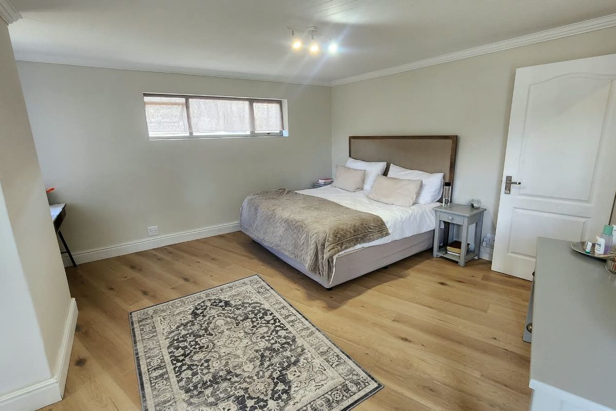 A well-maintained bedroom featuring light-toned laminate flooring, neutral wall finishes, and a horizontal window providing natural light.