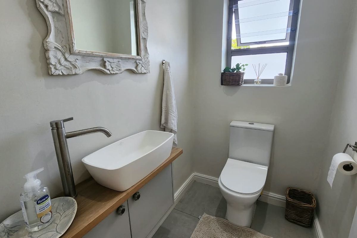 A modern guest bathroom featuring a vessel sink on a wooden vanity, a white toilet, and neutral tiled flooring.
