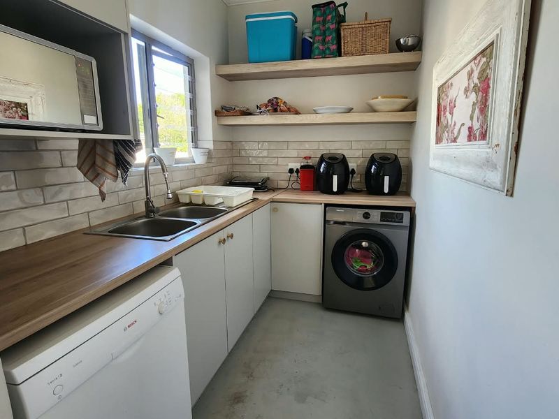 A functional scullery featuring wooden countertops, subway tile backsplash, double sink, and ample built-in cabinetry with open shelving for storage.