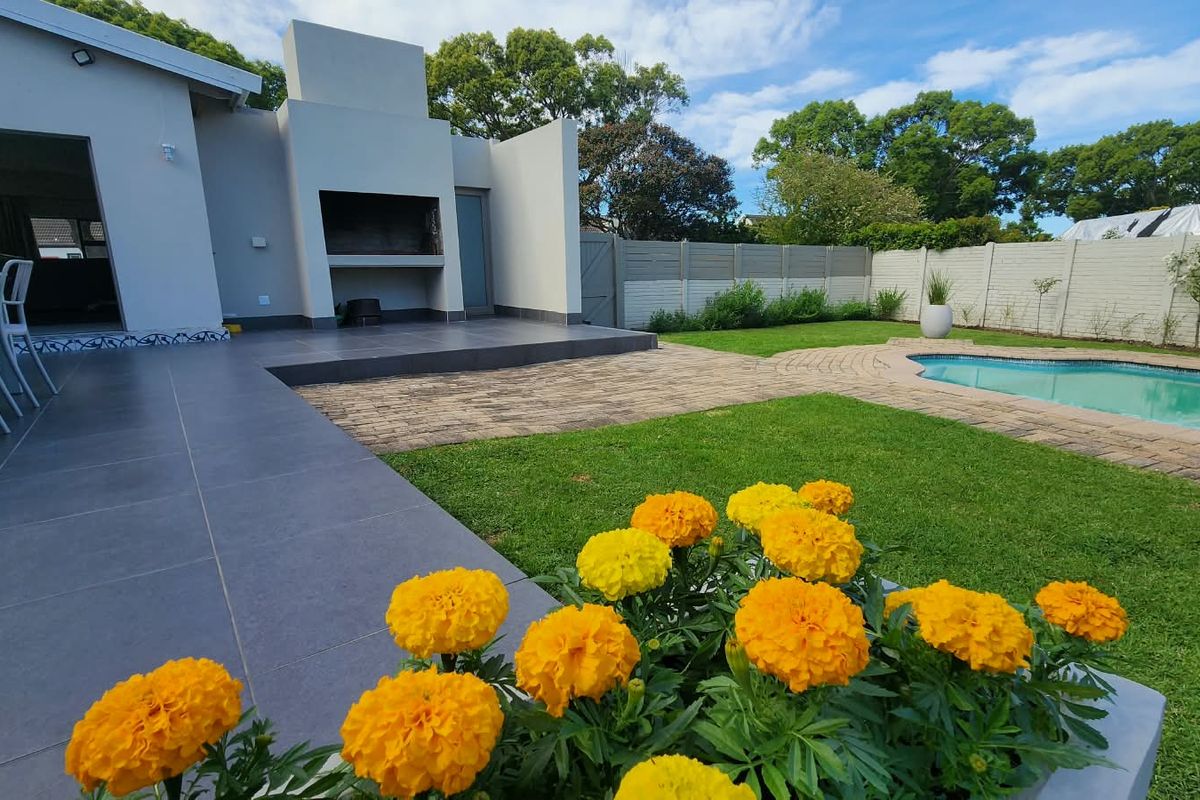 A well-maintained rear garden featuring a tiled patio with a built-in braai, a swimming pool with paved surround, and a secure boundary wall.