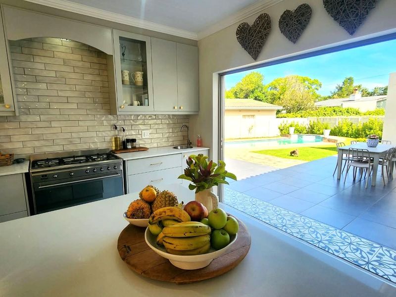 Modern kitchen featuring light grey cabinetry, subway tile backsplash, and a gas stove, with seamless flow to an outdoor patio and pool area.