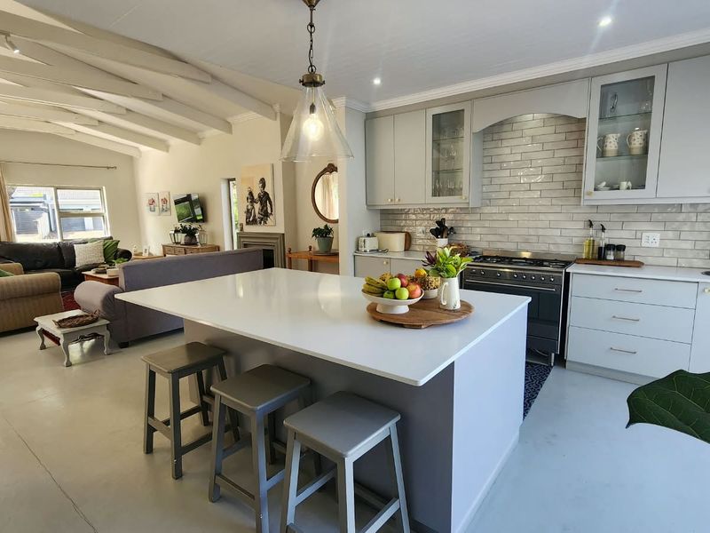 Spacious open-plan living area featuring a modern kitchen with a central island, quartz countertops, subway tile backsplash, and exposed ceiling beams.