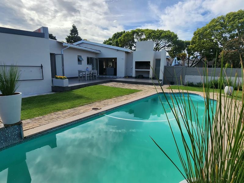 Outdoor entertainment area featuring a swimming pool, paved patio, and a built-in braai, set within a well-maintained garden.